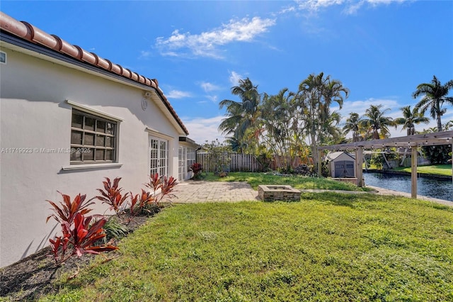 view of yard with a patio, a water view, fence, an outdoor structure, and a shed