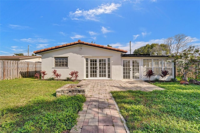 rear view of property featuring french doors, a tile roof, stucco siding, a lawn, and fence