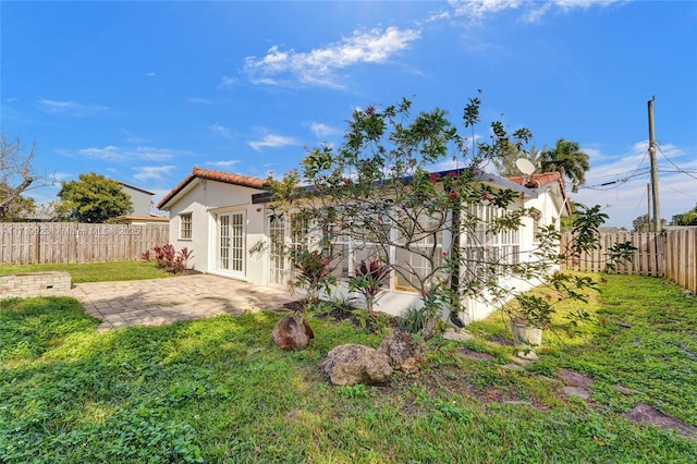 rear view of property featuring a tile roof, a yard, stucco siding, a patio area, and a fenced backyard