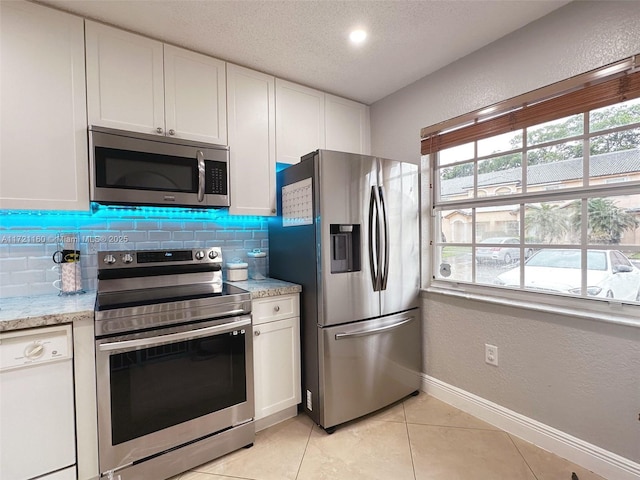 kitchen with backsplash, light stone countertops, light tile patterned flooring, white cabinetry, and stainless steel appliances