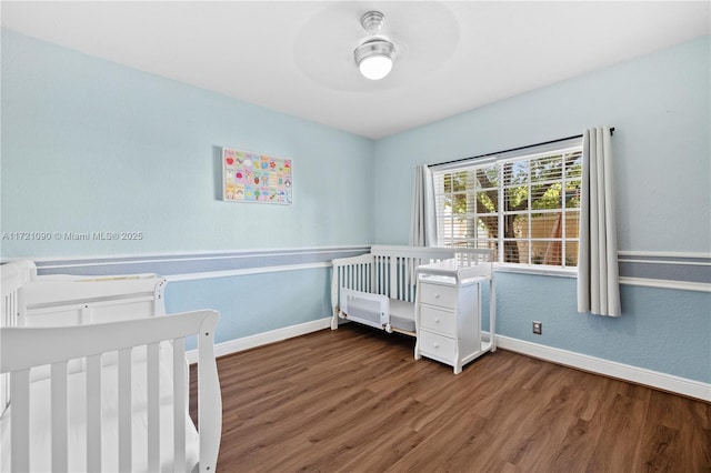 unfurnished bedroom featuring ceiling fan, a crib, and dark wood-type flooring