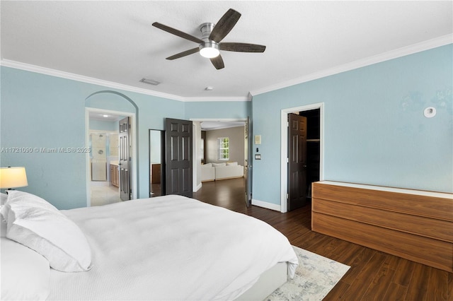 bedroom with dark wood-type flooring, a walk in closet, ensuite bath, ceiling fan, and ornamental molding