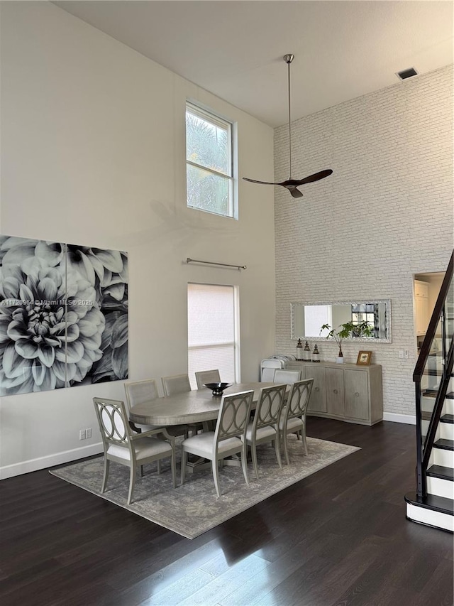 dining room featuring dark hardwood / wood-style flooring, a towering ceiling, and brick wall