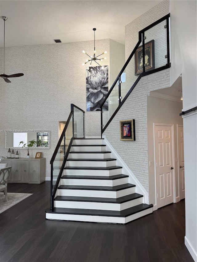 stairs featuring hardwood / wood-style flooring, brick wall, and a towering ceiling