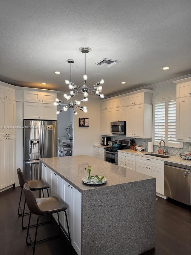 kitchen with decorative light fixtures, white cabinetry, sink, a center island, and stainless steel appliances