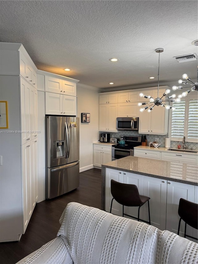 kitchen with appliances with stainless steel finishes, sink, dark stone counters, and white cabinets