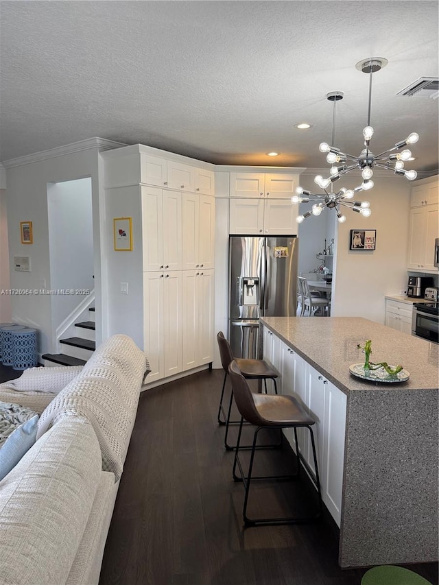 kitchen with a kitchen island, appliances with stainless steel finishes, white cabinets, hanging light fixtures, and ornamental molding