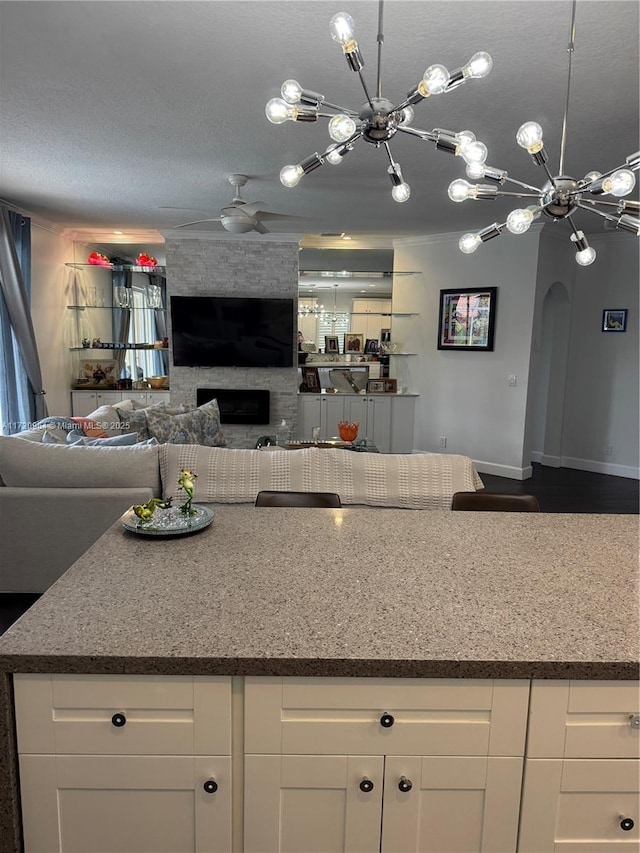 kitchen featuring white cabinetry, ceiling fan with notable chandelier, a fireplace, and a textured ceiling