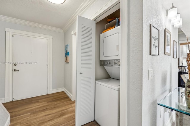 clothes washing area with stacked washer / dryer, light hardwood / wood-style flooring, a textured ceiling, and ornamental molding