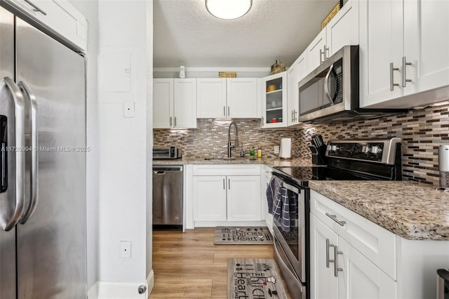 kitchen featuring backsplash, white cabinets, sink, light stone countertops, and appliances with stainless steel finishes