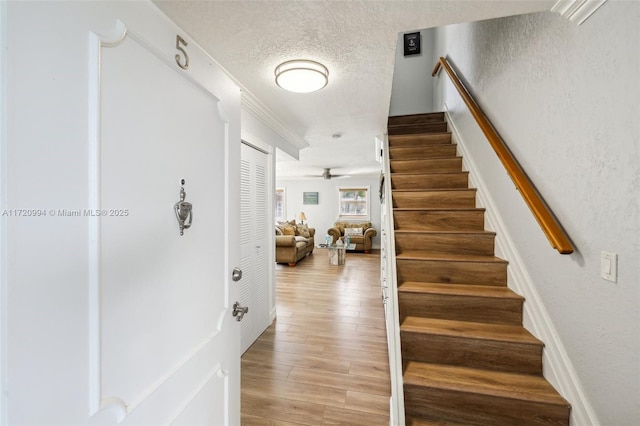 staircase with wood-type flooring, a textured ceiling, ceiling fan, and crown molding