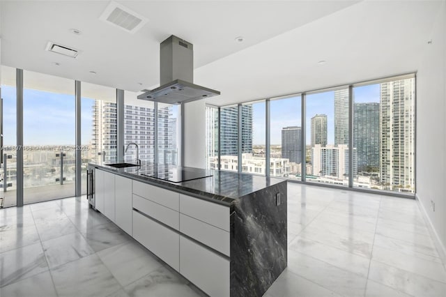 kitchen featuring white cabinetry, a wall of windows, island exhaust hood, dark stone countertops, and a spacious island