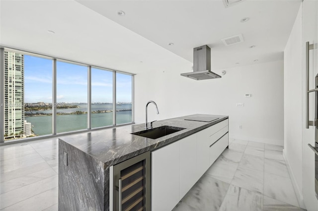 kitchen featuring white cabinetry, sink, beverage cooler, a kitchen island with sink, and a water view