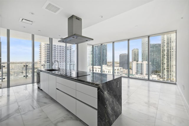 kitchen with white cabinetry, a wall of windows, island exhaust hood, dark stone countertops, and a large island with sink