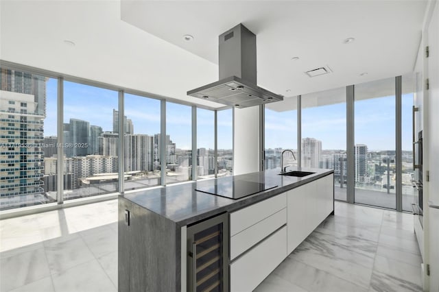 kitchen featuring sink, a wall of windows, island exhaust hood, a kitchen island with sink, and white cabinets