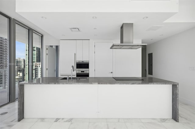 kitchen featuring white cabinets, a wall of windows, dark stone countertops, and exhaust hood