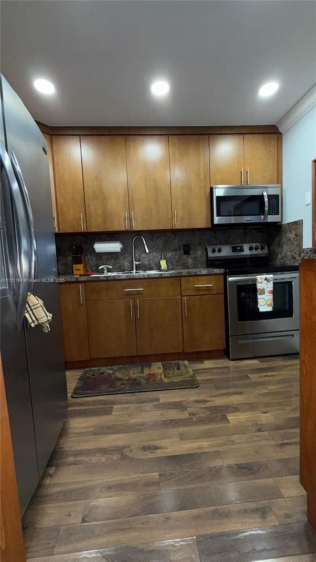 kitchen featuring dark wood-type flooring, stainless steel appliances, tasteful backsplash, dark stone countertops, and ornamental molding