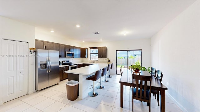 kitchen with a breakfast bar area, dark brown cabinetry, light tile patterned flooring, and stainless steel appliances