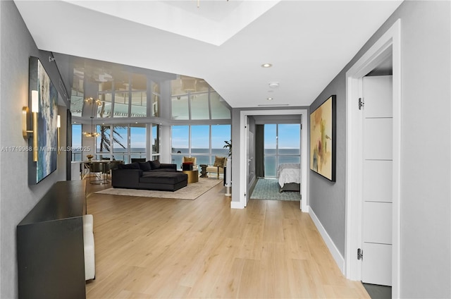 corridor with floor to ceiling windows, a water view, and light wood-type flooring