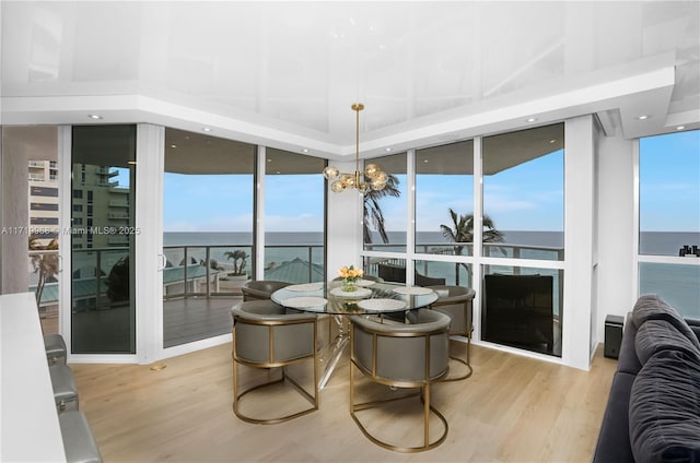 dining room featuring expansive windows, light hardwood / wood-style flooring, a water view, and a chandelier