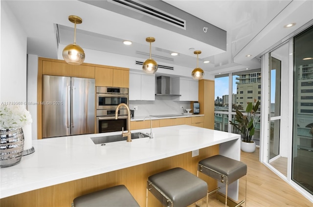 kitchen with white cabinetry, wall chimney range hood, kitchen peninsula, decorative light fixtures, and appliances with stainless steel finishes