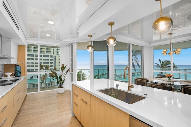 kitchen featuring light brown cabinets, black electric stovetop, a water view, sink, and decorative light fixtures