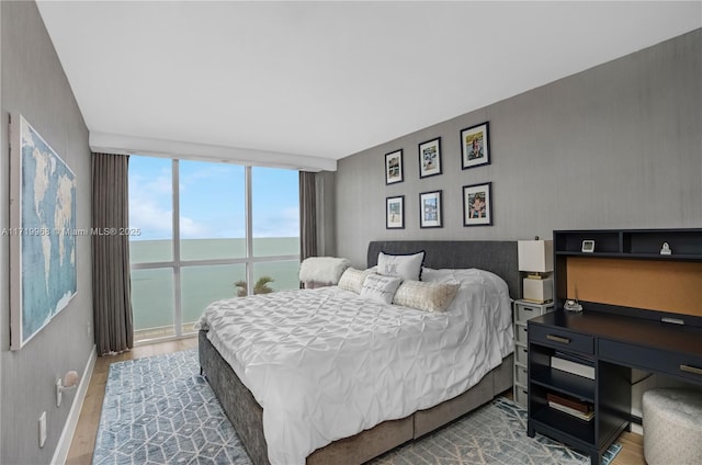 bedroom featuring floor to ceiling windows, a water view, and wood-type flooring