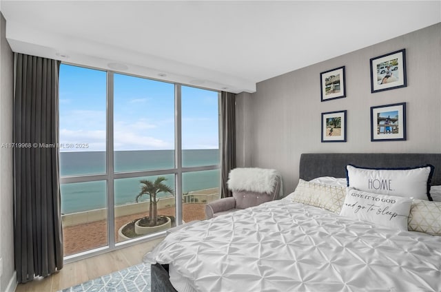 bedroom featuring hardwood / wood-style floors, a water view, and a wall of windows