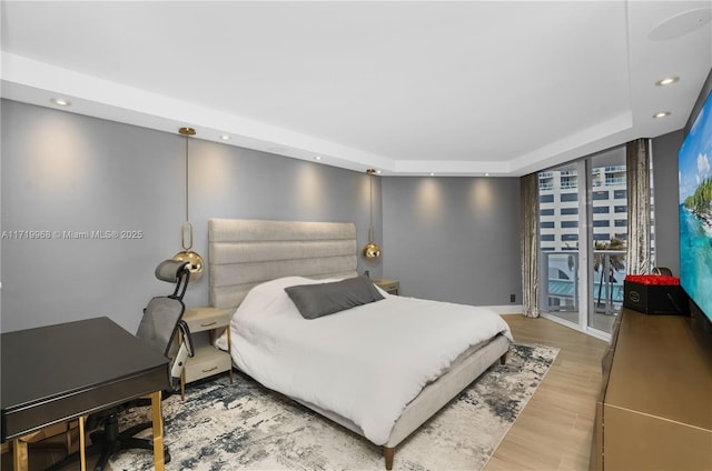 bedroom with a tray ceiling, access to exterior, hardwood / wood-style floors, and a wall of windows