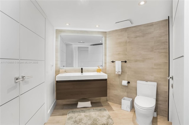 bathroom featuring vanity, tile walls, and toilet