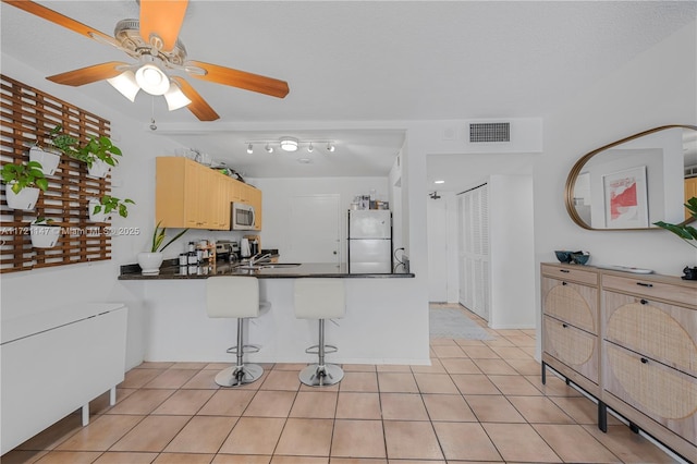 kitchen with visible vents, dark countertops, stainless steel microwave, freestanding refrigerator, and light brown cabinets