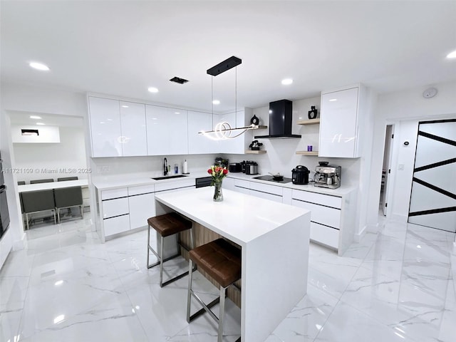 kitchen featuring a center island, white cabinetry, a kitchen breakfast bar, decorative light fixtures, and wall chimney exhaust hood