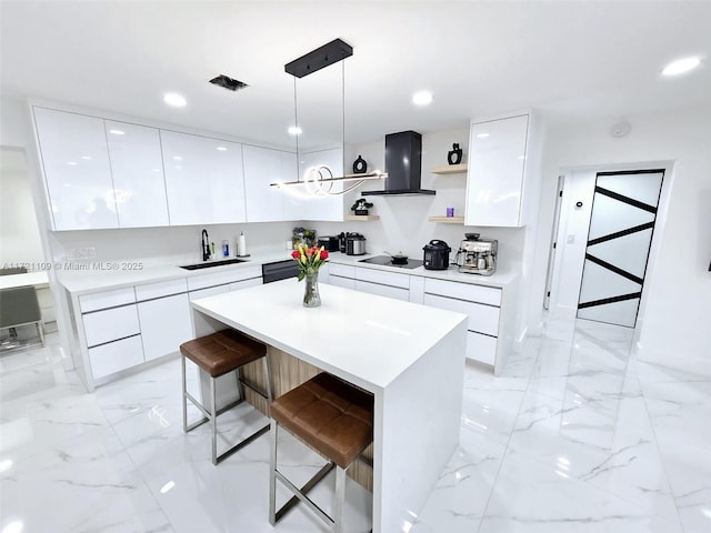 kitchen with a breakfast bar, sink, pendant lighting, wall chimney range hood, and white cabinets