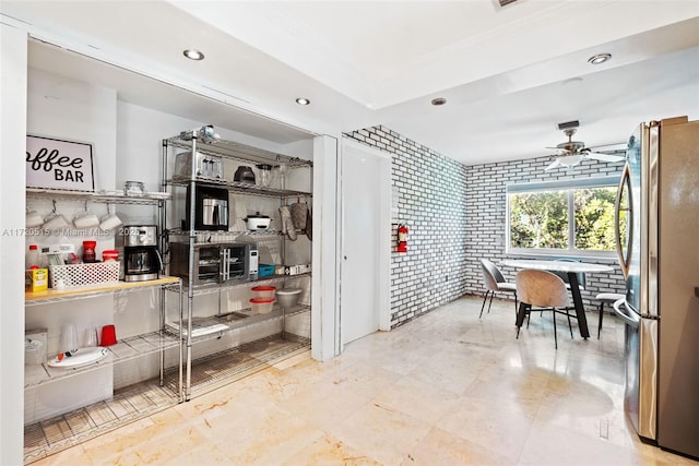 kitchen with backsplash, stainless steel refrigerator, ceiling fan, and brick wall