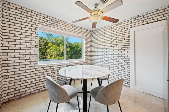 dining area featuring ceiling fan and brick wall