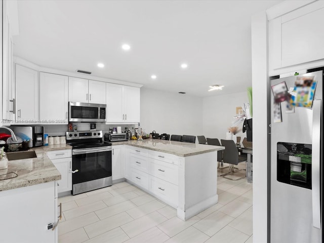 kitchen featuring kitchen peninsula, light tile patterned floors, appliances with stainless steel finishes, light stone counters, and white cabinetry