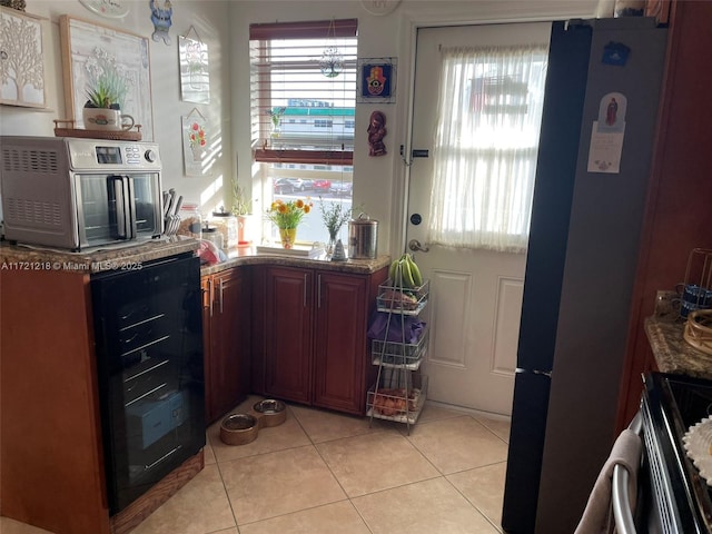 kitchen featuring stove, light tile patterned floors, beverage cooler, and dark stone counters