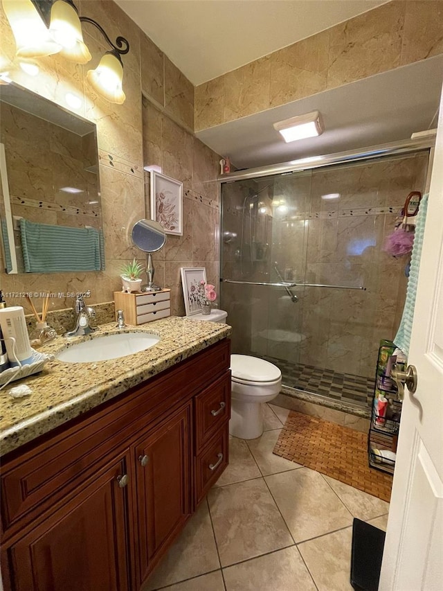 bathroom with tile patterned floors, toilet, a shower with shower door, and tile walls