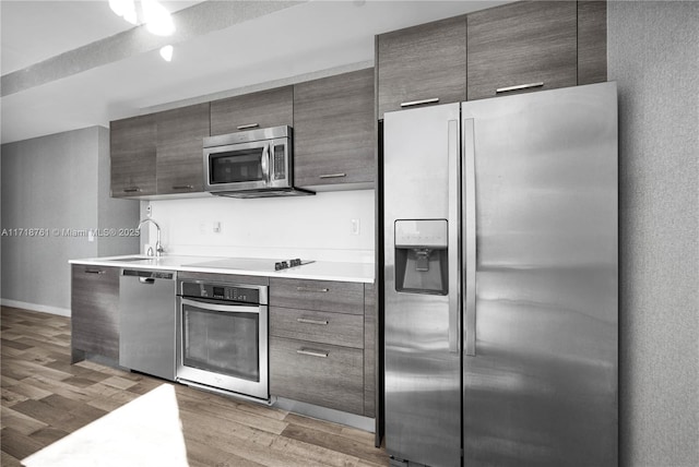 kitchen with light wood-type flooring, appliances with stainless steel finishes, sink, and dark brown cabinets