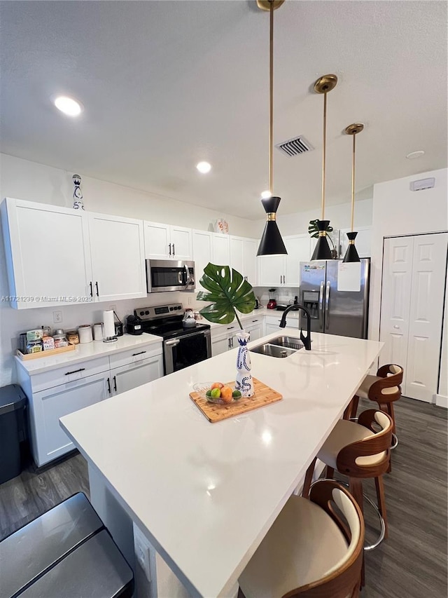 kitchen featuring appliances with stainless steel finishes, sink, white cabinets, hanging light fixtures, and a center island with sink