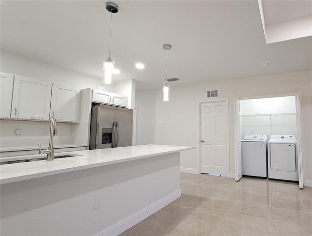 kitchen with light stone counters, stainless steel refrigerator with ice dispenser, independent washer and dryer, decorative light fixtures, and white cabinets