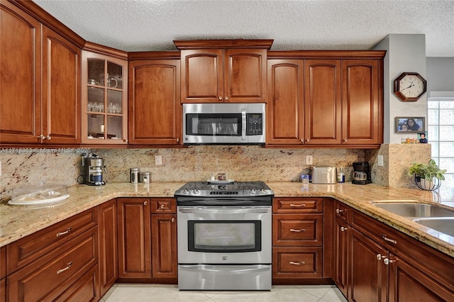 kitchen featuring light stone countertops, backsplash, a textured ceiling, stainless steel appliances, and light tile patterned floors