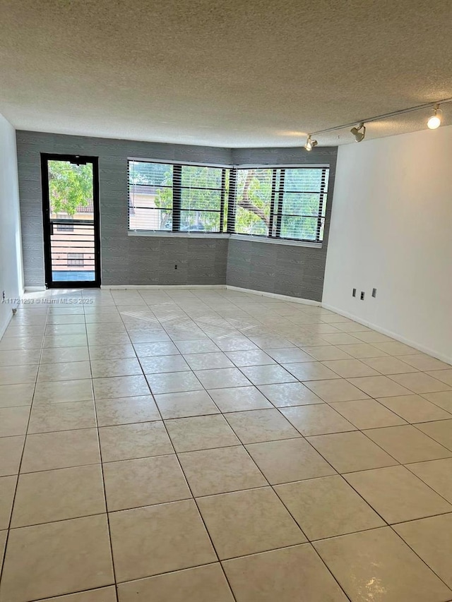 tiled empty room featuring rail lighting, a textured ceiling, and baseboards