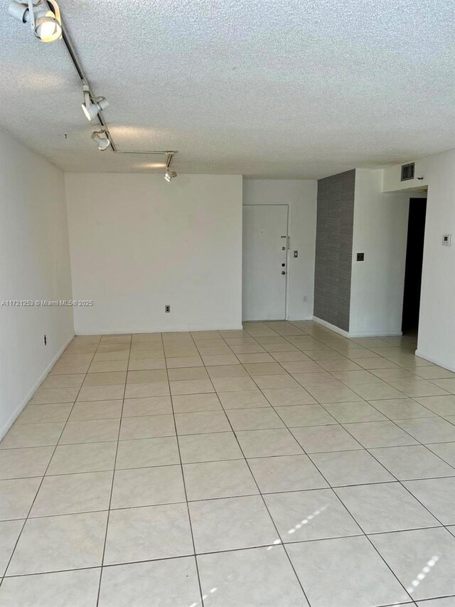 tiled empty room featuring rail lighting and a textured ceiling