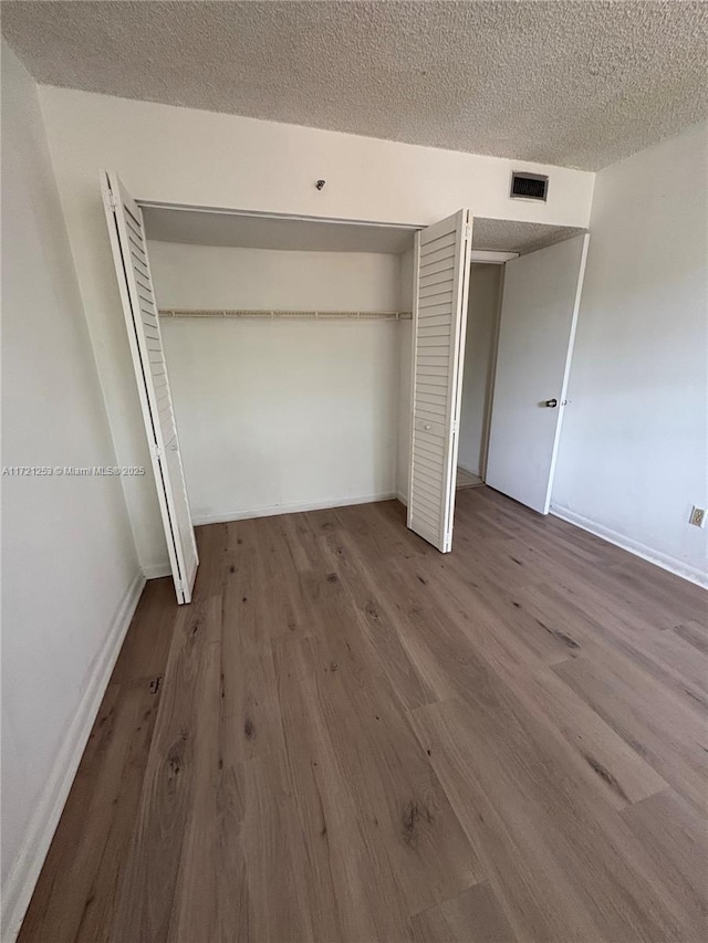 unfurnished bedroom featuring visible vents, a textured ceiling, wood finished floors, a closet, and baseboards