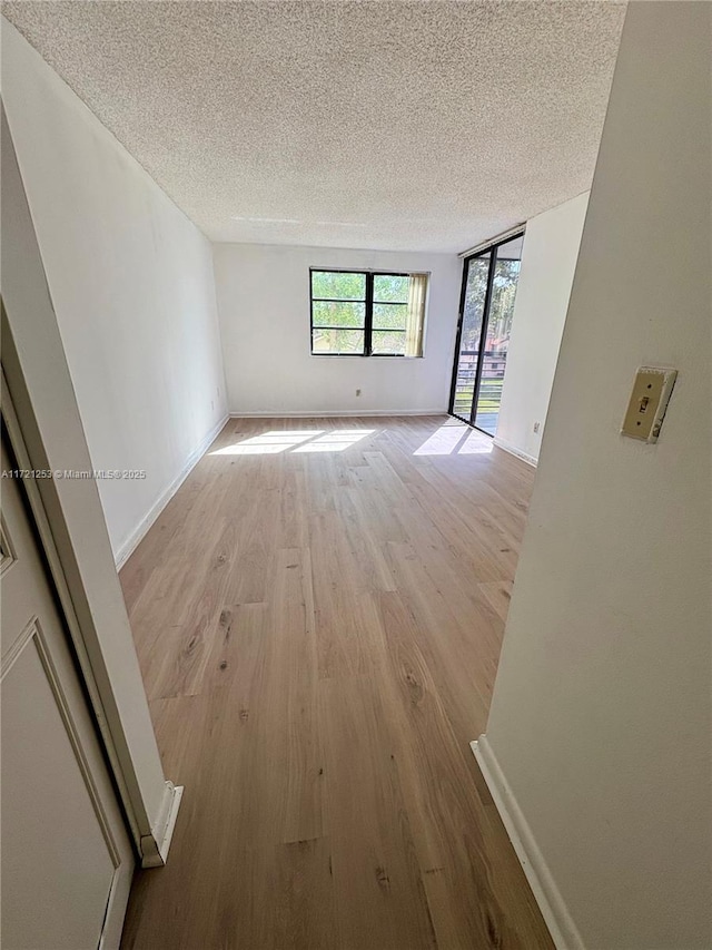 unfurnished room with baseboards, a textured ceiling, and light wood finished floors