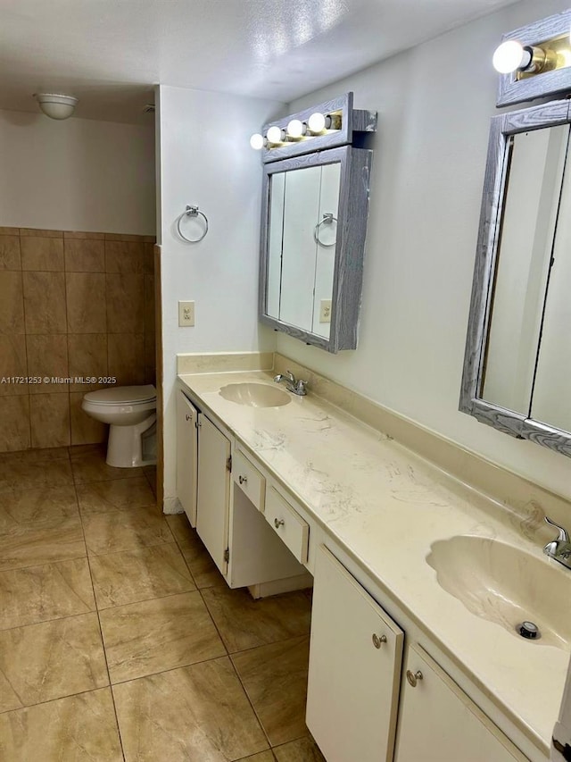 full bathroom with a sink, toilet, tile walls, and double vanity