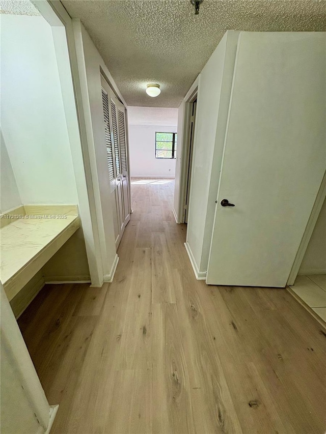 hallway featuring baseboards, light wood-type flooring, and a textured ceiling