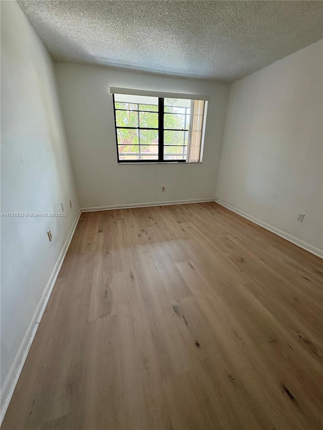 unfurnished room with light wood finished floors, a textured ceiling, and baseboards