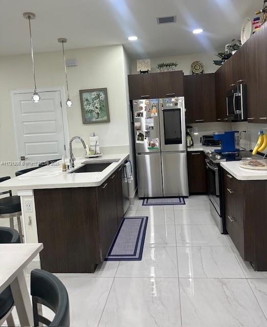 kitchen with stainless steel appliances, dark brown cabinets, pendant lighting, a breakfast bar, and sink